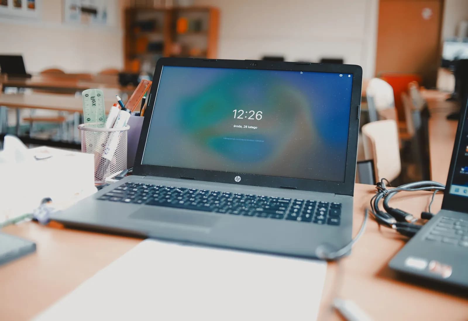 An open laptop on a classroom desk, more desks and machines out of focus behind it