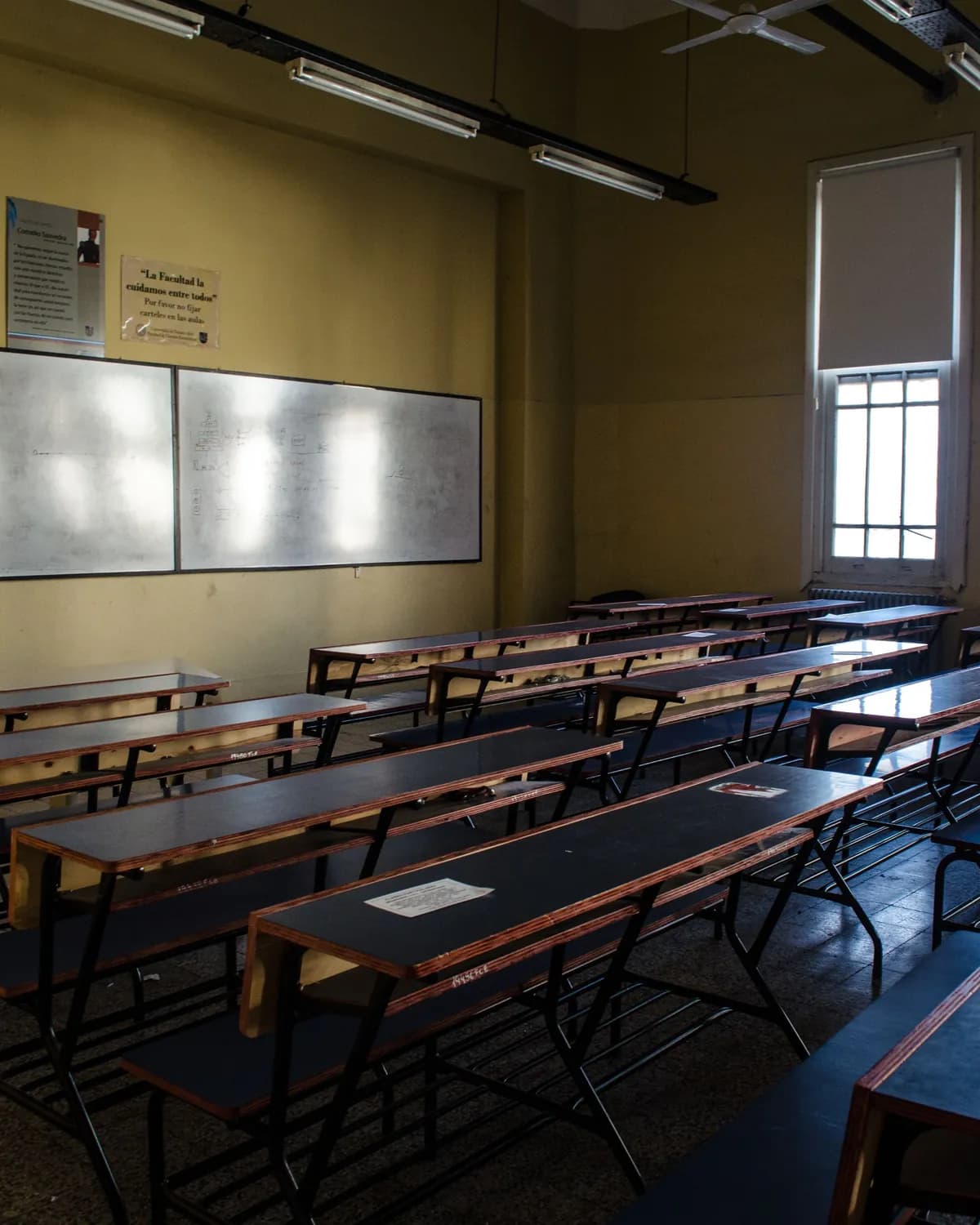 An empty teaching room in low light, long rows of desks facing a whiteboard
