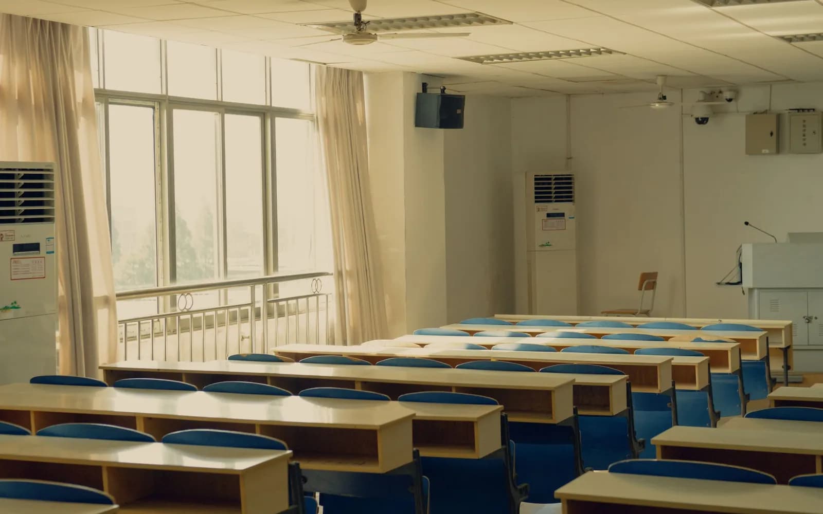 A wide teaching room, rows of desks along a wall of windows, nobody present