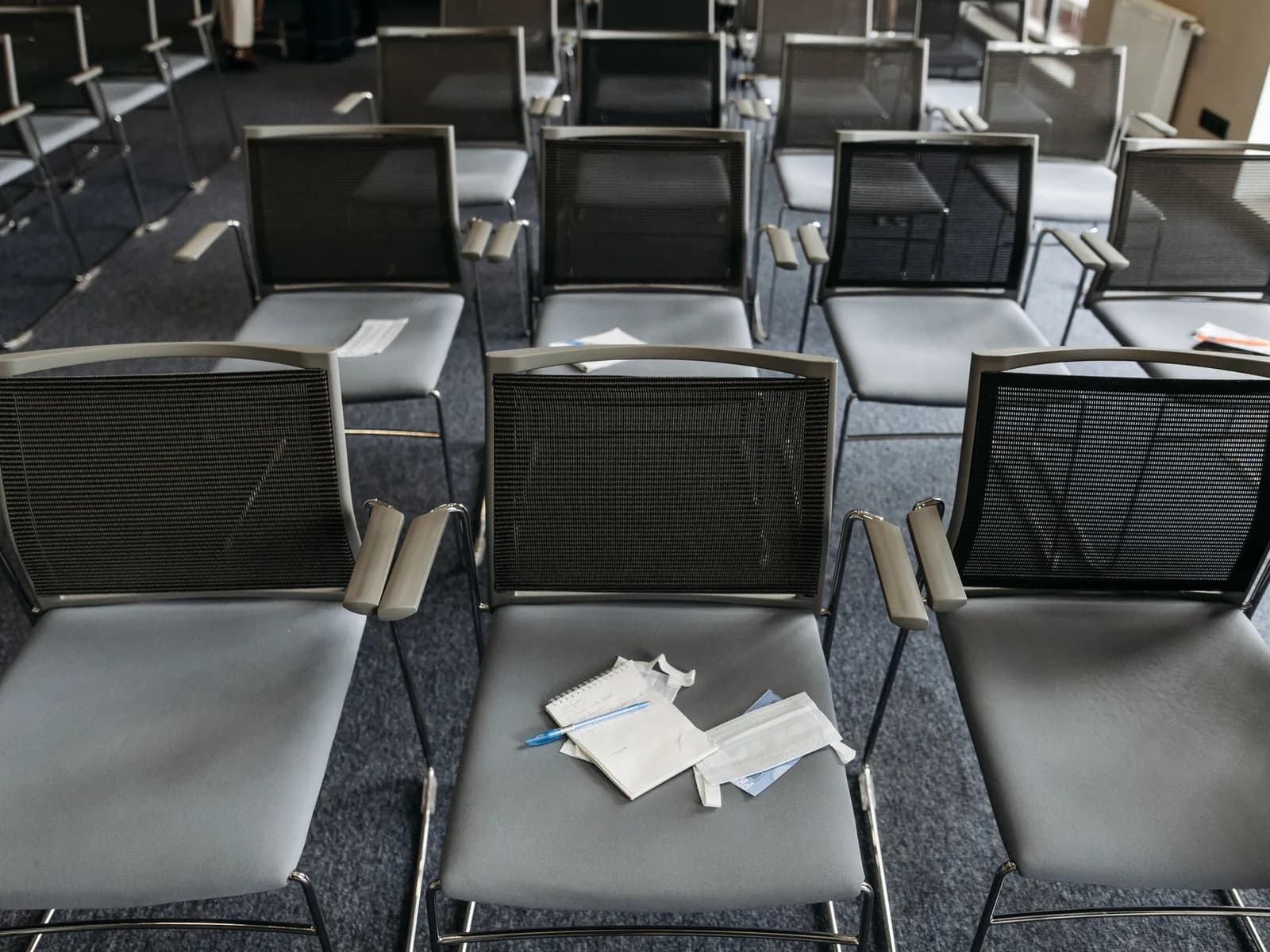 Rows of grey chairs seen from above, a few sheets of paper left behind on the seats